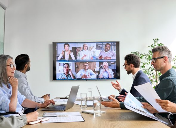 Diverse employees on online conference video call on tv screen in meeting room.